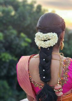 a woman with long black hair and flowers in her hair, wearing a pink sari