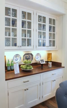 a kitchen with white cabinets and wooden counter tops, plates on top of the cupboards