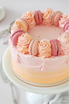 a cake with pink frosting and macaroons on top sitting on a plate