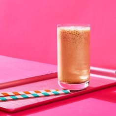 a drink sitting on top of a pink tray next to a glass with a straw in it