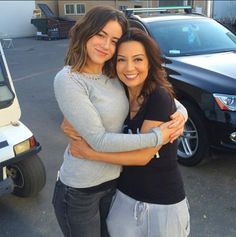 two women hugging each other in front of a car