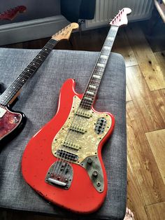 two electric guitars sitting on top of a gray cushion in front of a radiator