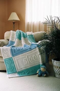 a crocheted blanket sitting on top of a couch next to a potted plant