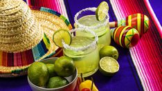 two margaritas with limeade, an avocado and a straw hat on a colorful table cloth