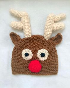 a crocheted reindeer hat with red nose and antlers on the top, sitting on a white surface