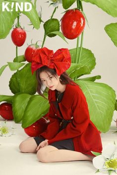 a young woman sitting on the ground in front of plants and flowers with red bows