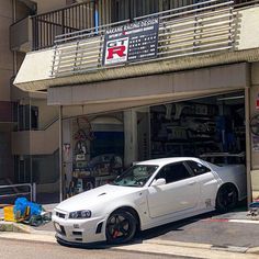 a white car is parked in front of a repair shop on the side of the road