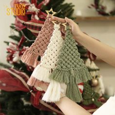 a person holding up some tassels in front of a christmas tree with decorations on it