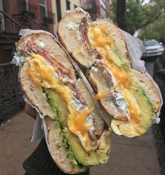 a person holding two sandwiches with meat and cheese on them in front of some buildings