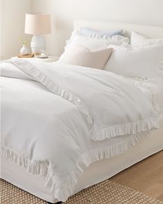 a bed with white linens and ruffled bedspread