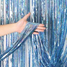 a woman's hand holding onto a blue curtain with silver tinsel on it