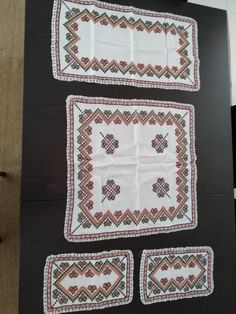 three pieces of embroidered cloth are displayed on a black surface with white and red designs