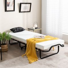 a bed sitting in the middle of a living room next to a table with a yellow blanket on it