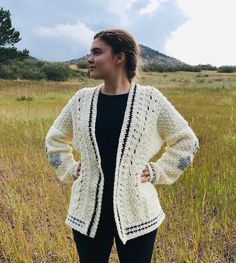 a woman standing in a field wearing a white crochet jacket and black leggings