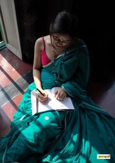 a woman in a green sari writing on a piece of paper