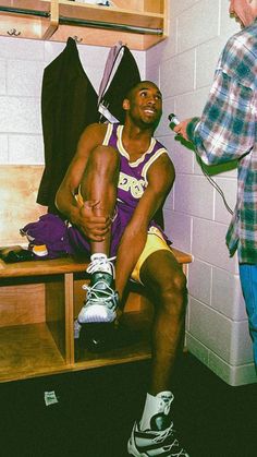 a man sitting on top of a bench in a locker room next to another man