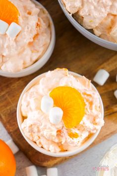 two bowls filled with orange fluff and marshmallows on top of a wooden cutting board