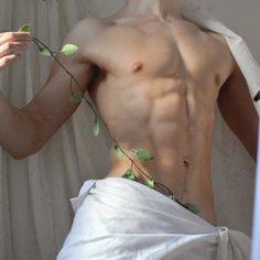 a man with no shirt on standing in front of a curtain and holding a plant