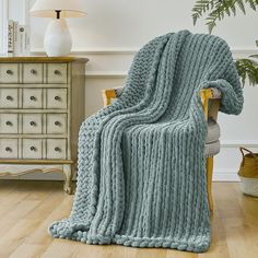 a blue blanket sitting on top of a chair next to a white dresser and potted plant