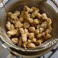 a metal basket filled with fried food on top of a stove burner and cooking utensils