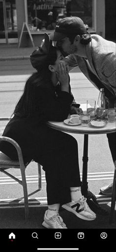 two people sitting at a table kissing each other