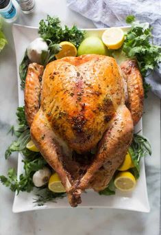 a roasted turkey on a white platter with lemons, parsley and herbs