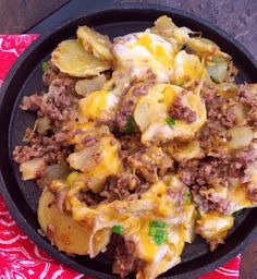 a skillet filled with potatoes, meat and cheese on top of a red table cloth