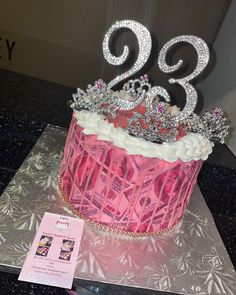 a pink cupcake with white frosting and tiara on top sitting on a table