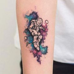 an astronaut tattoo on the arm with space and stars in the background, as well as watercolor paint