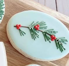 two decorated cookies sitting on top of a cutting board next to each other, one with red berries and the other green