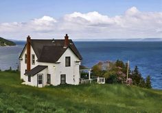 a white house sitting on top of a lush green hillside next to the ocean with mountains in the background