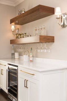 a kitchen with white cabinets and wine glasses on the shelf above the oven, which is built into the wall