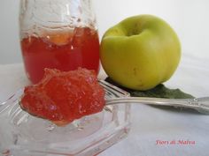 an apple and jelly sit next to each other on a table with a spoon in front of it