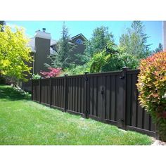 a fence in front of a house with trees and bushes on the side of it