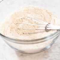 a glass bowl filled with flour and whisk on top of a white counter