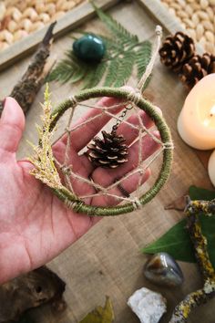 a hand holding a small piece of string with a pine cone on it, surrounded by other items