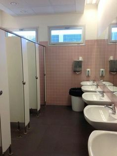 a public bathroom with pink tile walls and white sinks, urinals and stalls