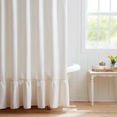 a white shower curtain with ruffles on it in a bathroom next to a window