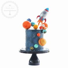 a space themed birthday cake with planets and rockets on top, sitting on a black pedestal