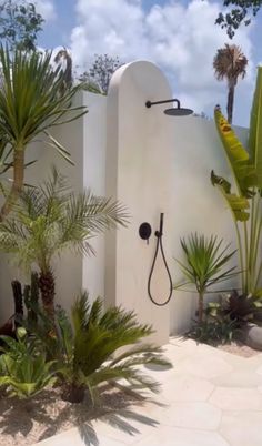 an outdoor shower surrounded by palm trees and other tropical plants on the side of a house