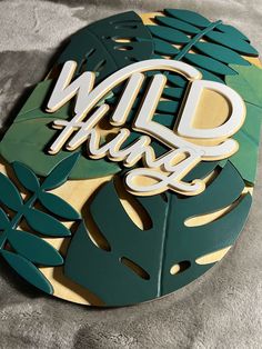 a wooden sign that says wild things with leaves and palm trees around it on a gray blanket