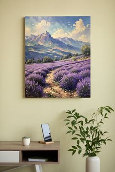 a painting hanging on the wall above a desk with a laptop and potted plant