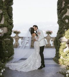 a bride and groom kissing in front of an arch covered with greenery on their wedding day