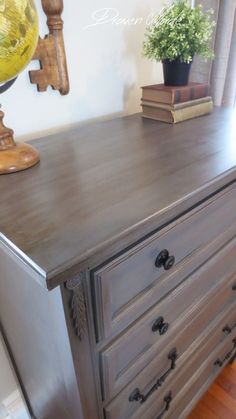 an old dresser is painted gray and has some books on the top, along with a potted plant