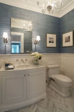 a bathroom with blue walls and white fixtures on the vanity, along with a chandelier