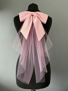 If you don't want a full veil how about this pretty pink satin hair bow with  and tulle veiling tails. A finishing touch that says bride but is a lot more modern.  The bow is 24cm long by 7cm  The silk tails measures 21cm to the longest point. With the tulle 46cm from the bow.  All mounted on a hair comb which can be slipped into your hair do and pinned into place. This lovely hair bow will go with loads of wedding dress styles even trouser suits and mini dresses and just a touch for colour for