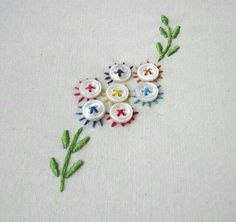 embroidered flowers on white fabric with green stems and small button holes in center, surrounded by smaller buttons