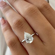 a woman's engagement ring with a pear shaped diamond in the center, on her finger