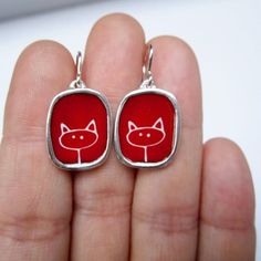 This simple line drawing captures the essence of a cute kitty.  The white line drawing is on a bright red vitreous enamel background.Handmade from sterling silver and kiln fired enamel in my California workshop, they are 3/4 of an inch tall and dangle from solid sterling French ear wires. These are made to last a lifetime. Wear them every day! See some of my other enamel cat jewelry here:https://www.etsy.com/shop/marmar?ref=hdr_shop_menu&search_query=enamel+cat+jewelryTo see my entire store Cute Red Enamel Earrings, Red Hand Painted Sterling Silver Jewelry, Cute Hand Painted Red Jewelry, Cute Red Hand-painted Jewelry, Cute Red Hand Painted Jewelry, Simple Line Drawing, Hello Kitty Earrings, Simple Line Drawings, Vitreous Enamel