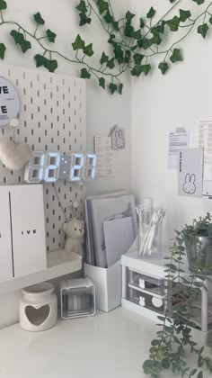 a white desk topped with lots of clutter next to a wall mounted clock and plant